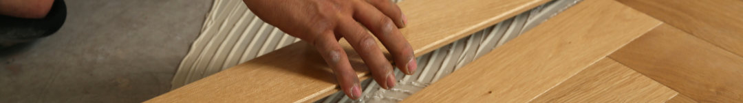Person installing wooden flooring on a floor with adhesive